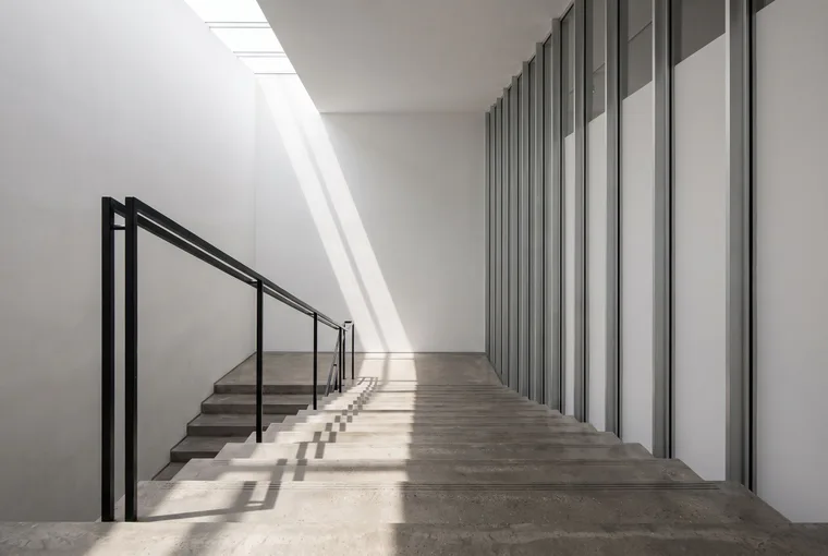 Un large escalier de béton qui descend sous la lumière d'un puits de jour.
